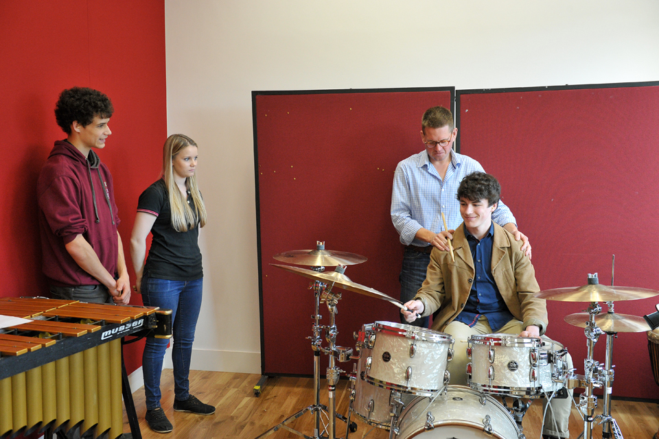 Two students observing one student having a drum kit lesson in the RCM's percussion suite